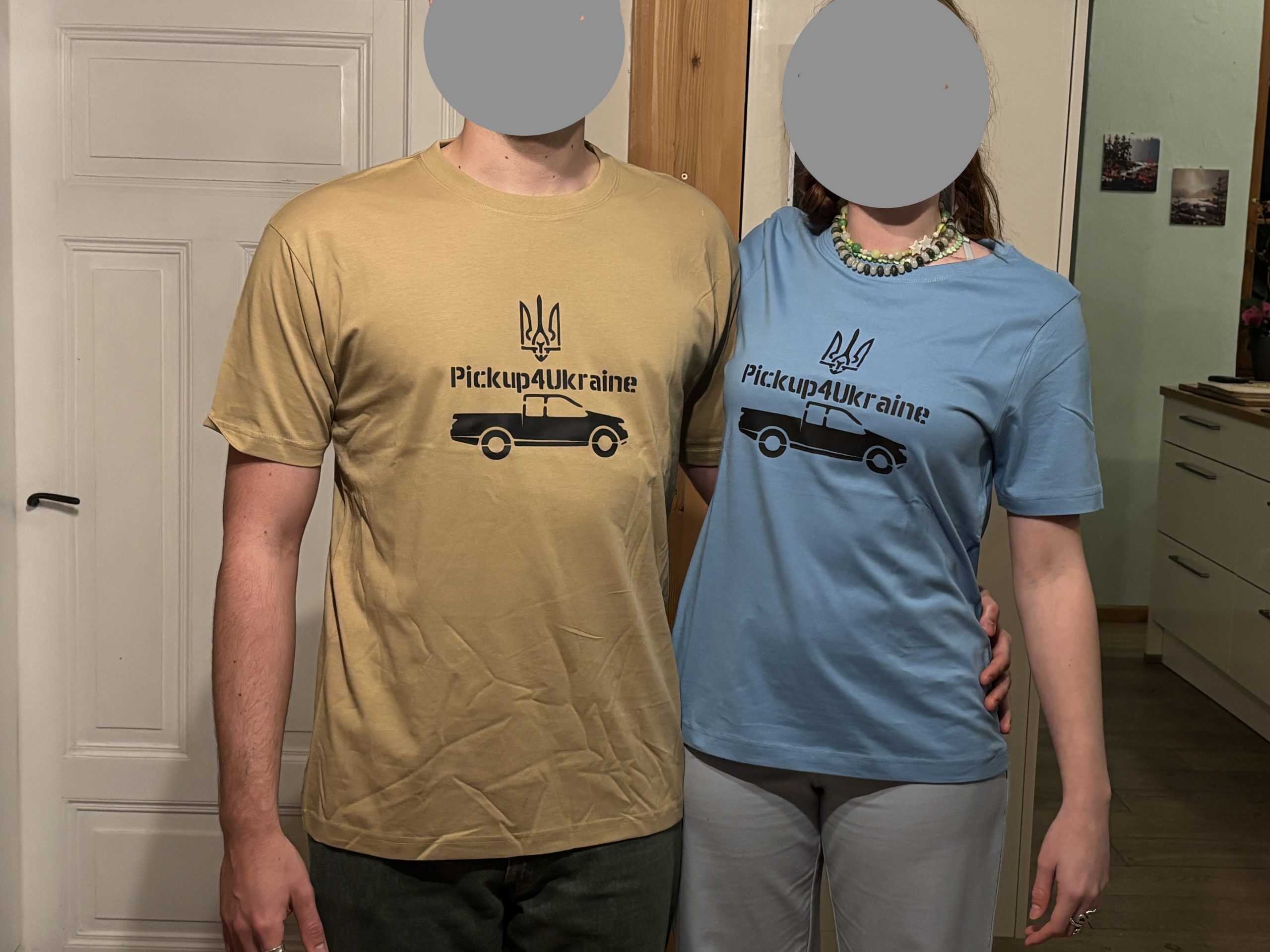 zwei Personen zeigen ein beiges und ein hellblaues T-Shirt mit dem Logo von Pickup4Ukraine